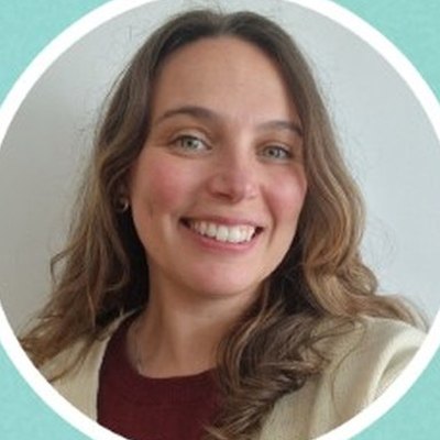Carmen Gonçalves, de cabelo castanho comprido e ondulado e casaco claro, sorri sobre fundo cinzento-claro.
