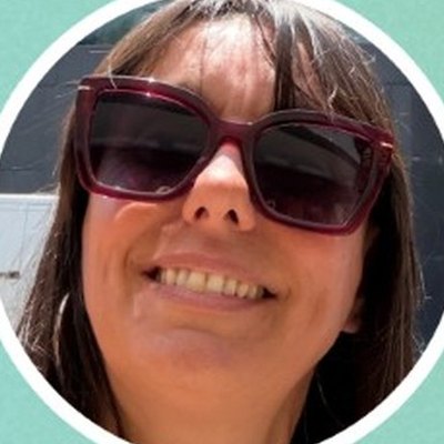 Elisabete Maciel, de franja e óculos de sol de armação bordeaux, sorri numa fotografia tirada de perto, ao ar livre.