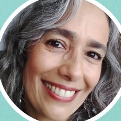 Grande plano de Juliana Nogueira, de cabelo comprido e grisalho ondulado e batom vermelho, com um sorriso largo.