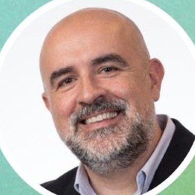 Luís Águeda, careca e de barba grisalha, com camisa clara e casaco escuro, sorri sobre fundo branco.