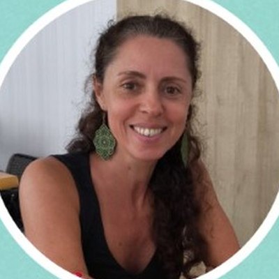 Raíssa Santos, de cabelo castanho apanhado, brincos verdes compridos e top preto, sorri sentada numa sala.