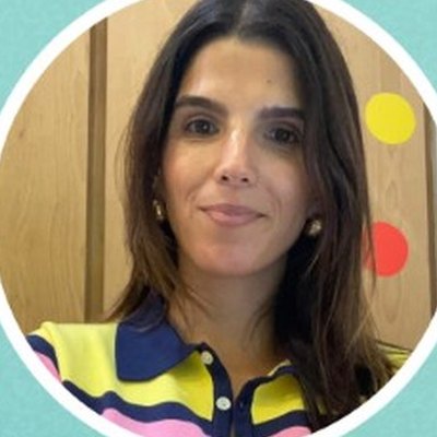 Teresa Aguiar, de cabelo escuro comprido e camisola às riscas coloridas, sorri numa sala com círculos coloridos na parede.