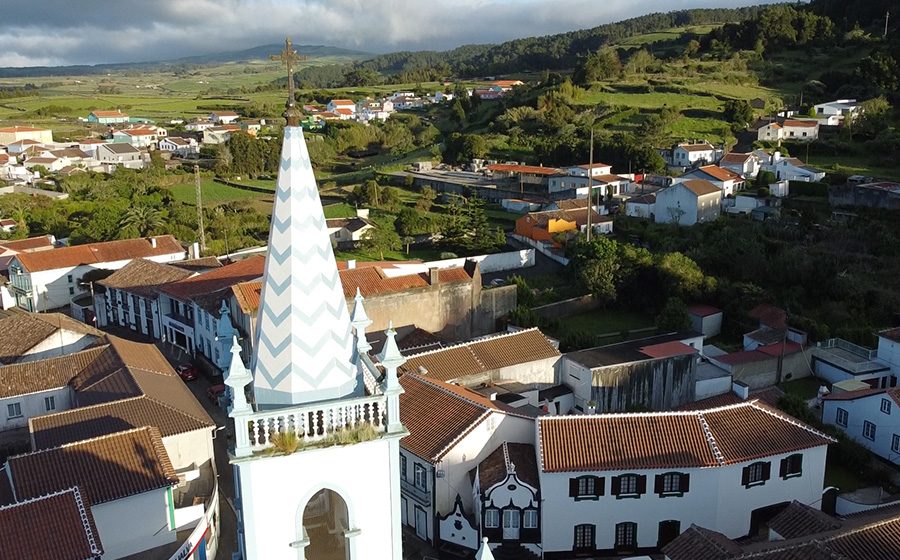 Vista aérea de uma freguesia rural da Ilha Terceira, com a igreja e casas de telhados vermelhos.