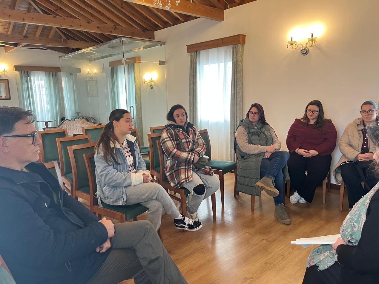 Pequeno grupo de jovens sentados em círculo numa sala com tetos de madeira, a ouvir quem fala.