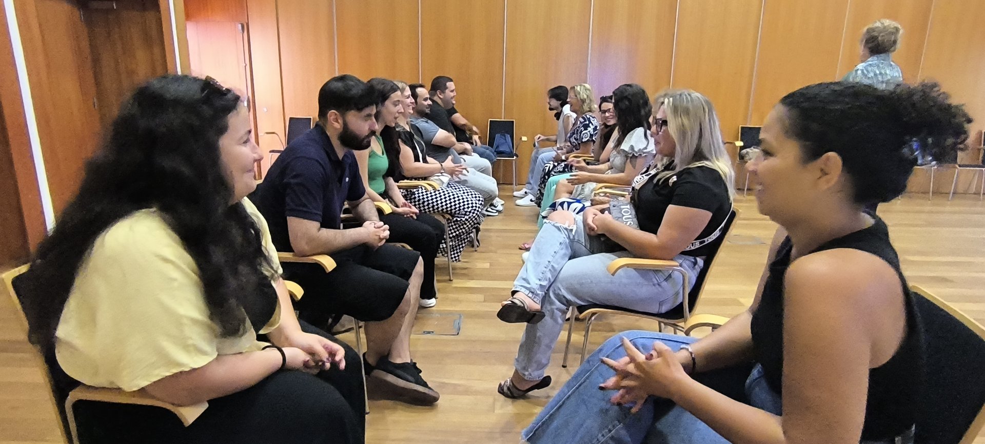 Participantes sentados em duas filas, frente a frente, praticam entrevistas em pares durante uma oficina.