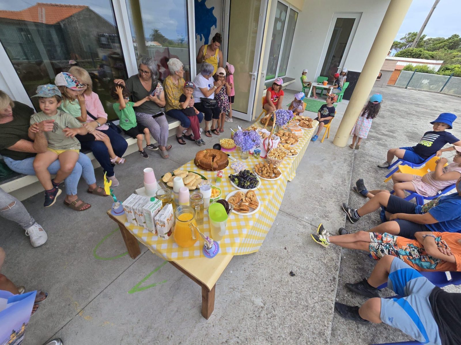 Avós e crianças sentados à volta de uma mesa de lanche ao ar livre.