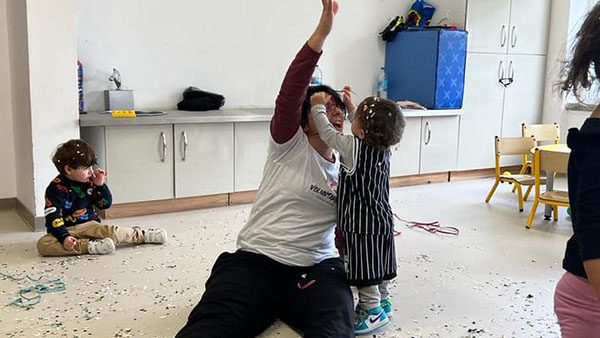 Voluntária brinca com duas crianças pequenas numa sala da creche.