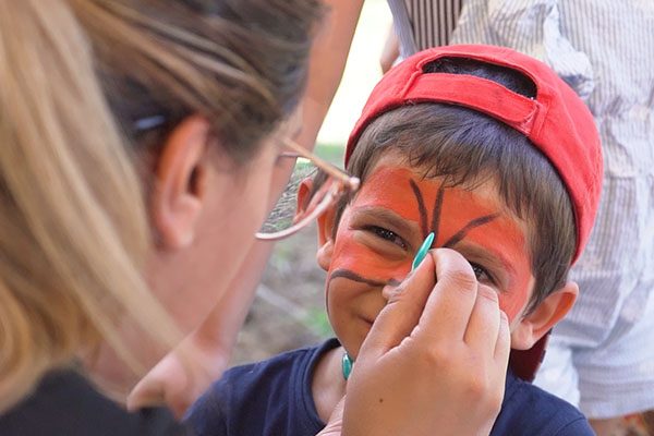 Animadora pinta a cara de um menino com boné vermelho.