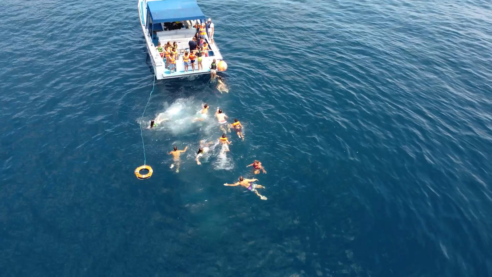 Vista aérea de crianças com coletes salva-vidas a nadar no mar junto a um barco.