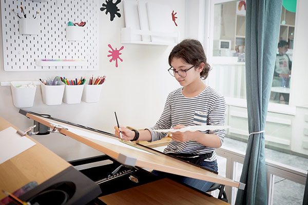 Jovem concentrado a desenhar numa secretária de um espaço de estudo luminoso.