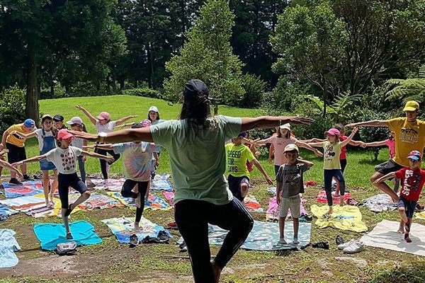 Grupo de crianças faz exercícios de equilíbrio ao ar livre num jardim.
