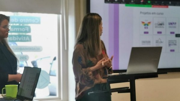 Formadora apresenta conteúdos num ecrã a um grupo numa sala de formação.