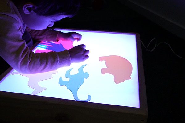 Criança explora formas coloridas numa mesa de luz.